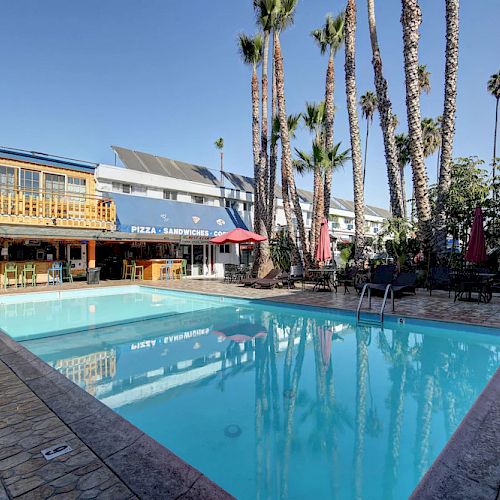 A poolside scene with palm trees, lounge chairs, and a building in the background, featuring a pizzeria and a bar area.