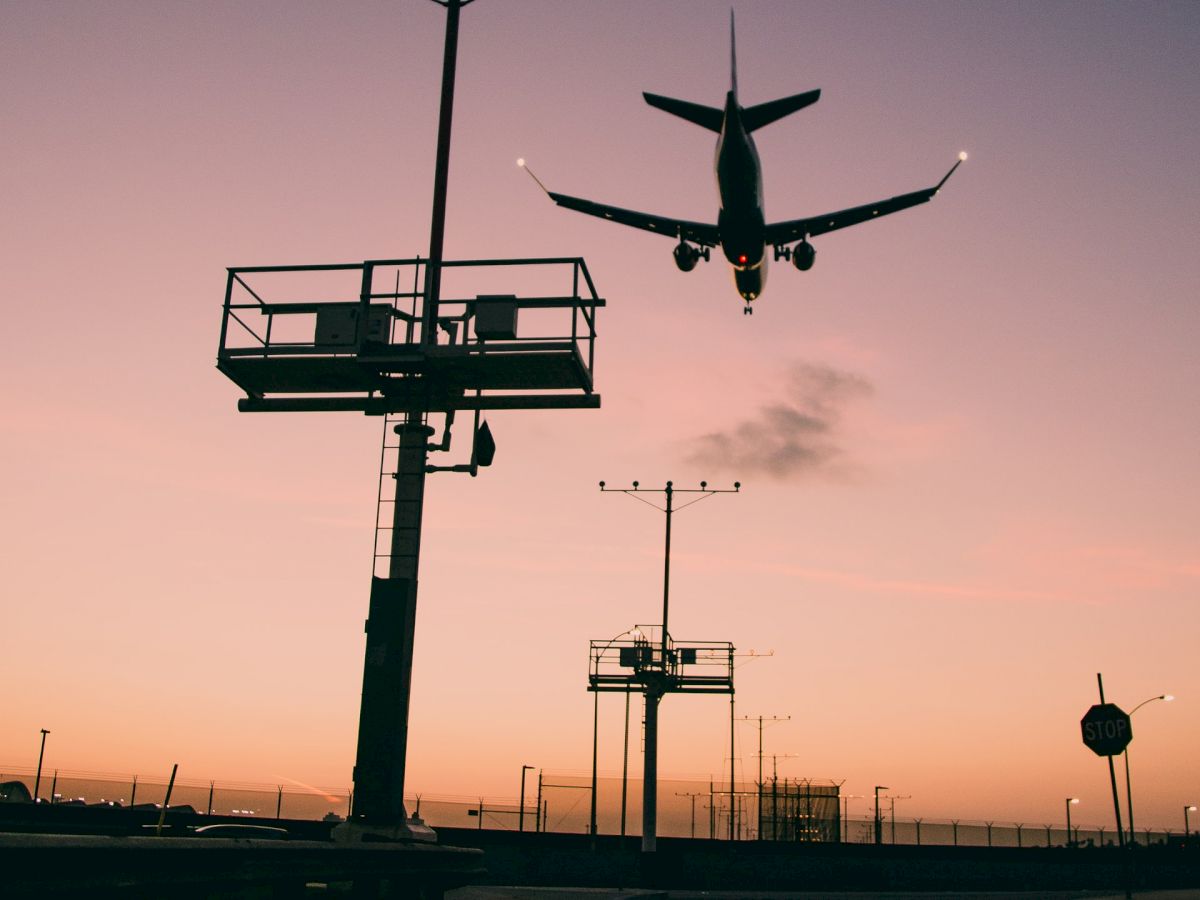 A plane is landing at dusk with a control tower and “STOP” road markings in the foreground, creating a dramatic silhouette against the pink sky.