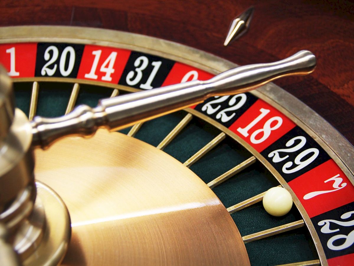 The image shows a roulette wheel with a ball landed on the red number 18. A metal arm is visible above the wheel.