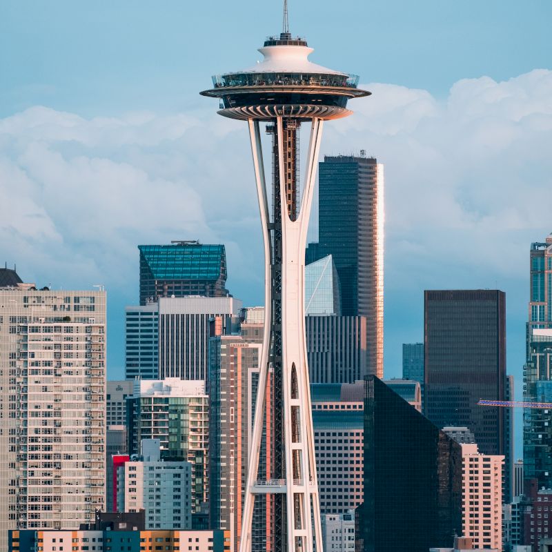 This image shows the Space Needle in Seattle, with a backdrop of various city buildings and a partly cloudy sky.