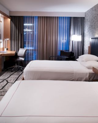 A hotel room with two neatly made beds, a wall-mounted TV, a desk by the window, and modern decor.