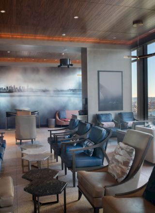 A modern lounge with numerous seating options, wall art of a city skyline, large windows offering waterfront views, and stylish interior design elements.