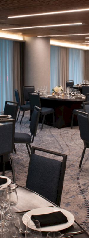 The image shows an elegant dining area set for an event or banquet, with round tables covered in black tablecloths, chairs, and sophisticated place settings.