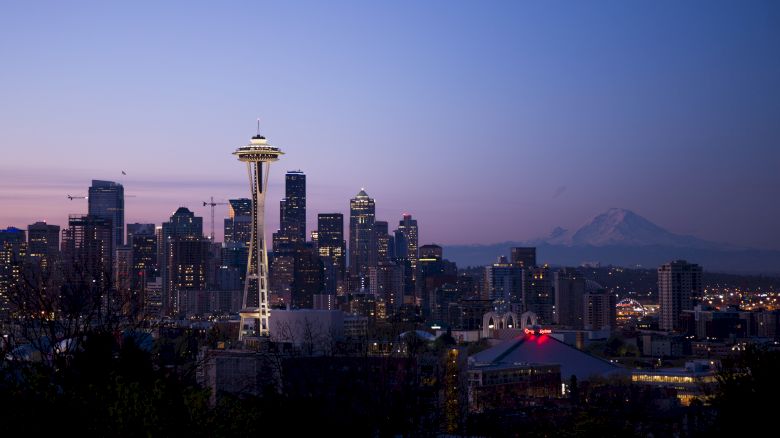 A view of the Seattle skyline at dusk, featuring the Space Needle, surrounding buildings, and Mount Rainier in the background, under a clear sky.