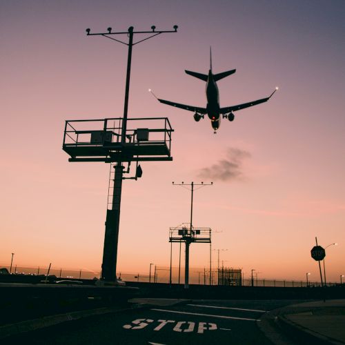 A plane is flying close to landing with airport structures and a sign marked 