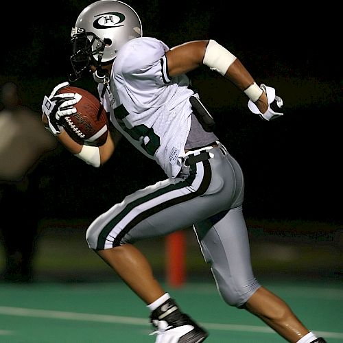 A football player in a gray and white uniform is running on a field while holding a football.